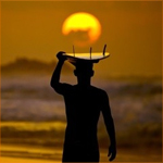 Мужчина с доской для серфинга на голове на фоне заката