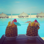Два коктейля в ананасах на фоне бассейна, пляжа и моря