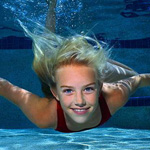 Улыбающаяся под водой в бассейне светловолосая девочка