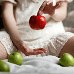 Девочка держит красное яблоко, рядом лежит зеленые яблоки
