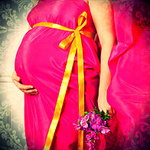 Беременная в розовом платье и с цветами в руке