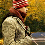 Парень в пальто, шарфе и шапке в осеннем лесу около дороги