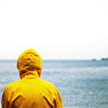 Парень в желтой куртке стоит у моря