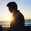 На фоне заходящего над морем солнца силуэт мужчины
