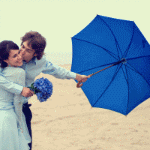 Парень с синим зонтом в одной руке и букетом в другой обн...