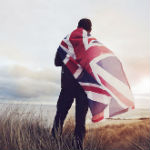 Парень с британским флагом на плечах стоит в поле