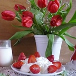 Букет тюльпанов стоит на столе рядом с тарелкой сливок и ...