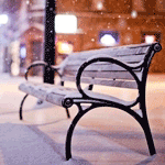  <b>Падающий</b> снег на заснеженную скамейку на городской улице 