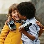 Мальчик с фотоаппаратом целует девочку с фотоаппаратом
