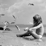 Маленькая девочка на берегу моря, рядом с ней чайки
