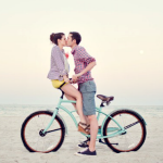 Пара целуется на велосипеде стоя на берегу моря